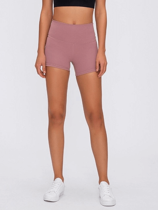 Woman wearing pink sports short elastic training shorts paired with white sneakers, showcasing a comfortable and stylish workout outfit.